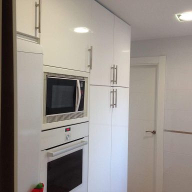 Cocina moderna con muebles blancos, horno y microondas empotrados.