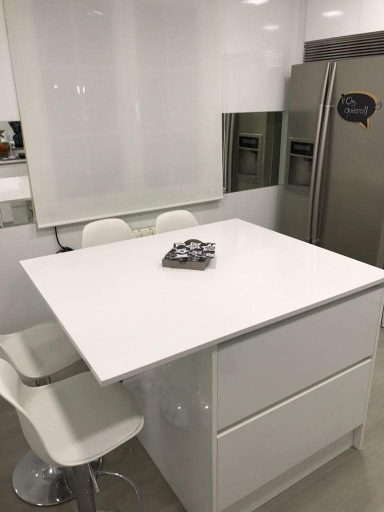 Cocina moderna con mesa blanca y sillas altas, electrodomésticos de acero inoxidable.