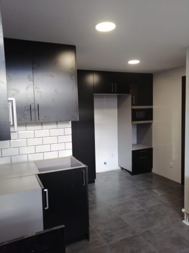 Cocina moderna con muebles oscuros y azulejos blancos en las paredes. Suelo de baldosas grises.