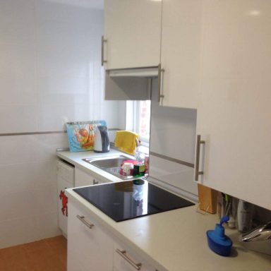 Cocina moderna con armarios blancos, encimera negra y ventana iluminando el espacio.
