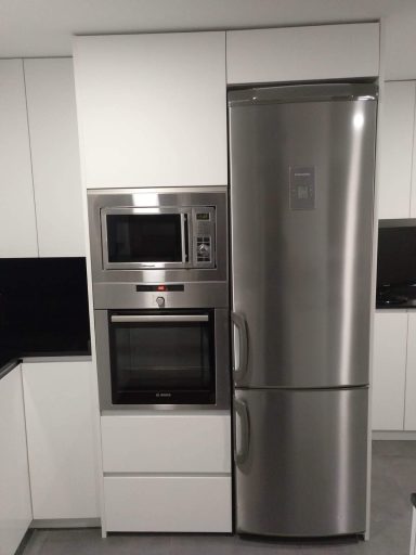 Cocina moderna con refrigerador y microondas integrados en un mueble blanco.