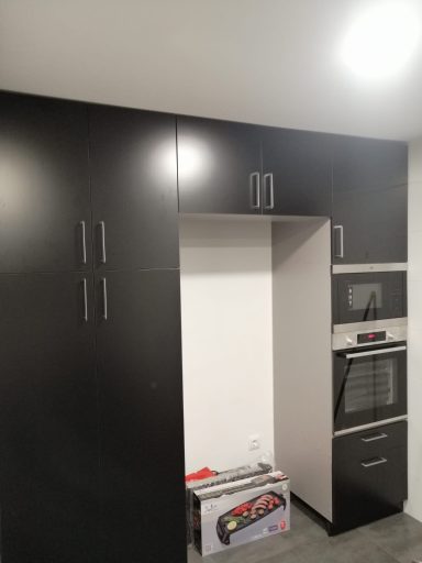 Cocina moderna con mobiliario negro, horno empotrado y espacio vacío.