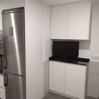 Cocina moderna con muebles blancos, nevera plateada y encimera negra.