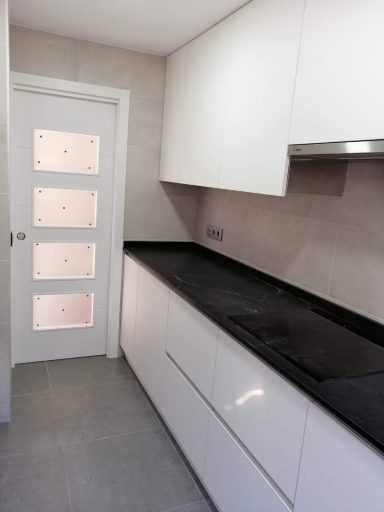 Cocina moderna con muebles blancos y encimera negra, puerta blanca al fondo.