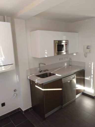 Cocina moderna con encimera de granito, muebles blancos y electrodomésticos integrados.