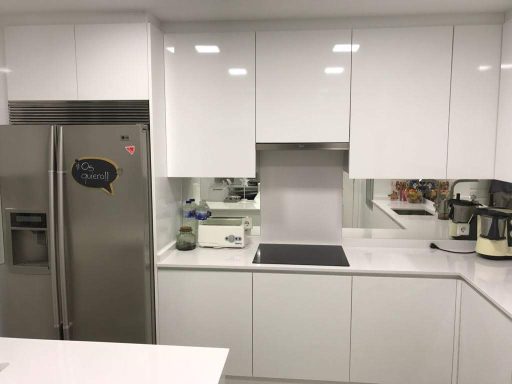 Cocina moderna con muebles blancos, electrodomésticos de acero inoxidable y encimera de mármol.