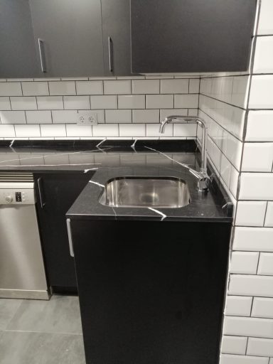 Encimera de cocina negra con fregadero de acero inoxidable y azulejos blancos.