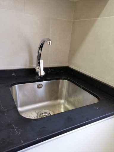 Fregadero cuadrado del acero inoxidable con grifo moderno sobre una encimera oscura.