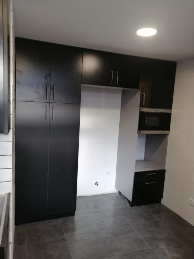Cocina moderna con muebles negros y área para microondas, paredes claras y suelo gris.