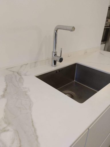 Fregadero de acero inoxidable con grifo moderno, sobre encimera de mármol.