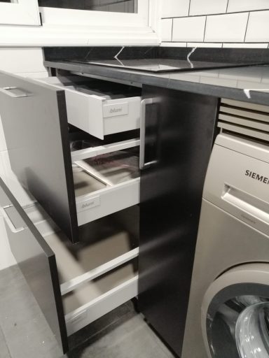 Puertas de un mueble de cocina con cajones abiertos y una lavadora al lado.