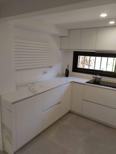 Cocina moderna con muebles blancos y superficies de granito, ventana al exterior.