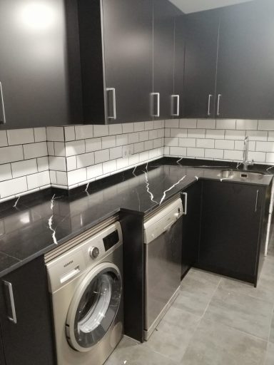 Cocina moderna con muebles oscuros, lavadora y lavavajillas integrados.