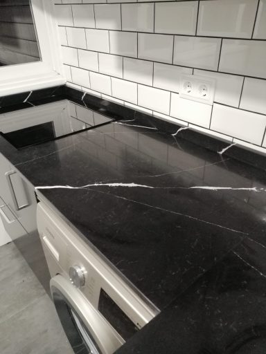 Encimera de cocina de granito negro con vetas blancas y azulejos de fondo.