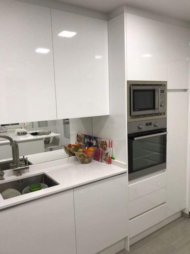 Cocina moderna con muebles blancos, horno empotrado y fregadero.