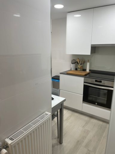 Cocina moderna con muebles blancos, horno, mesa y radiador.