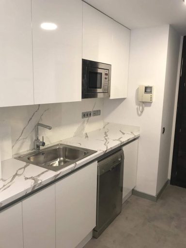 Cocina moderna con muebles blancos, fregadero, microondas y lavavajillas.