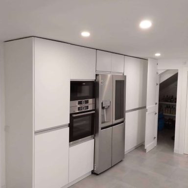 Cocina moderna con muebles blancos, nevera y horno empotrados. Suelo claro.