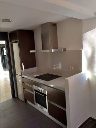 Cocina moderna con muebles oscuros, encimera blanca y electrodomésticos de acero inoxidable.