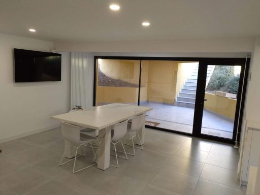 Interior moderno con mesa blanca, sillas transparentes y grandes ventanales.