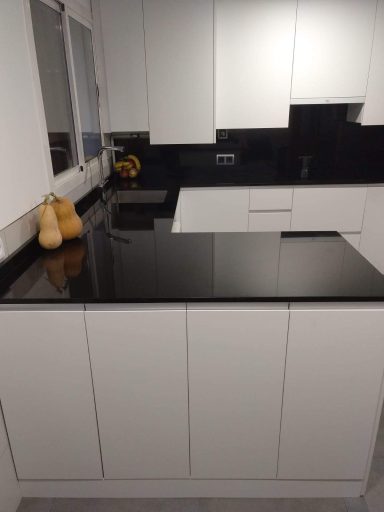 Cocina moderna con muebles blancos y encimera negra. Frutas en la parte superior.