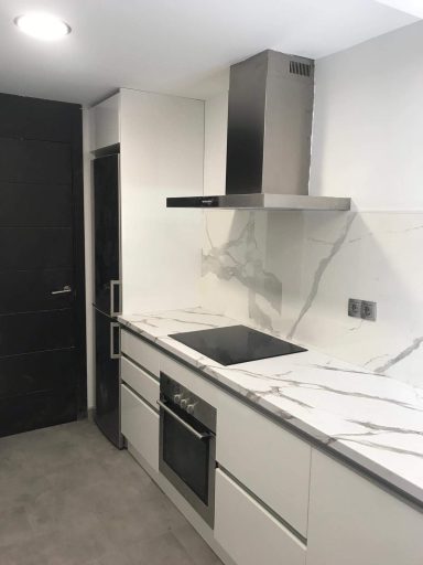 Cocina moderna con encimera de mármol y campana extractora. Puerta negra al fondo.