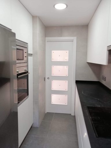 Cocina moderna con muebles blancos, pared gris y una puerta con ventanas de cristal.