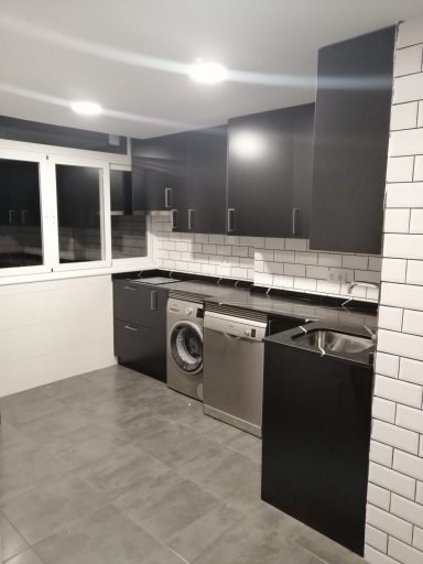Cocina moderna con muebles oscuros, lavadora y encimera de azulejos blancos.