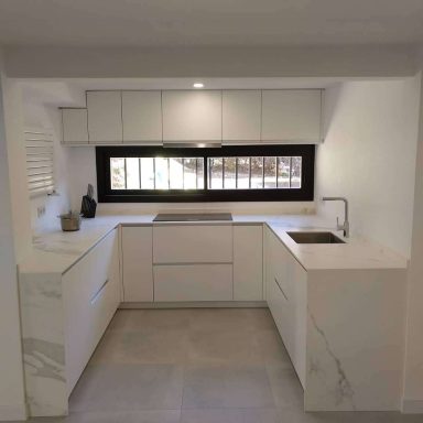 Cocina moderna con armarios blancos y una encimera de mármol, luz natural.
