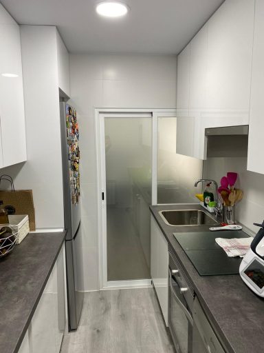 Cocina moderna con armarios blancos, encimera gris y puerta de vidrio hacia un área pequeña.