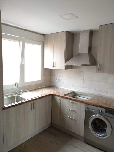 Cocina moderna con muebles de madera, lavadora y ventana iluminando el espacio.