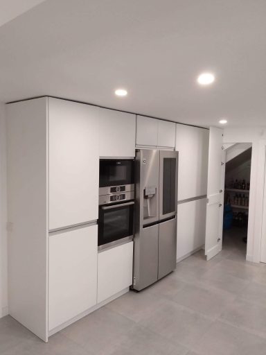 Cocina moderna con muebles blancos, horno y frigorífico integrados. Suelo de baldosas grises.