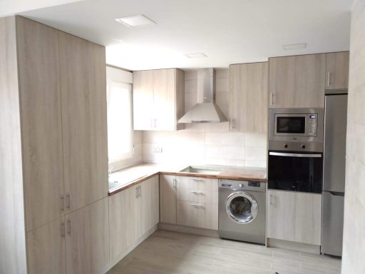 Cocina moderna con muebles de madera clara y electrodomésticos de acero inoxidable.