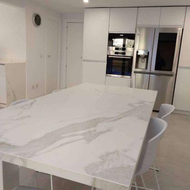 Cocina moderna con mesa blanca y sillas, electrodomésticos de acero y armarios minimalistas.