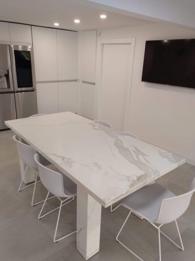 Mesa de comedor de mármol blanco con sillas blancas en una cocina moderna y luminosa.