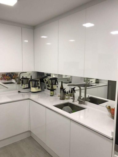 Cocina moderna con muebles blancos y fregadero, reflejos en la pared.